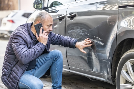 Man talks on the phone while inspecting the damage to his vehicle after a car accident
